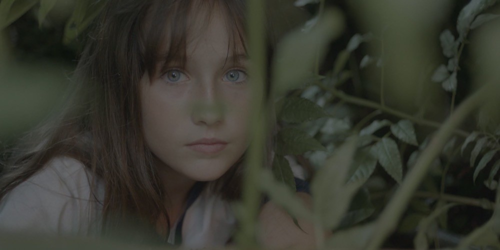 a white woman with brown hair and bangs blue eyes surrounded by tall plants