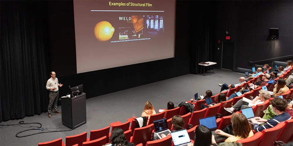 professor rob king teaching in front of project with students sitting in auditorium