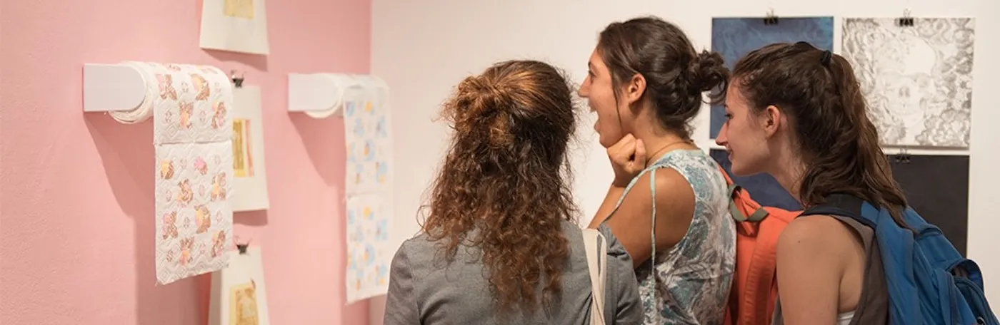 Three students view painted paper towels against a pink wall