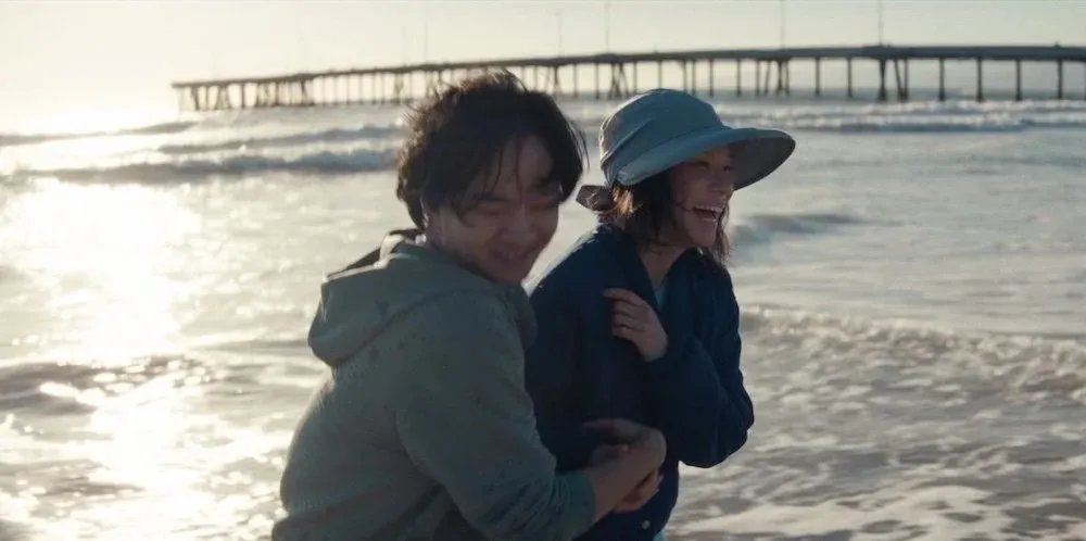 a mother and son walk arm-in-arm on the beach