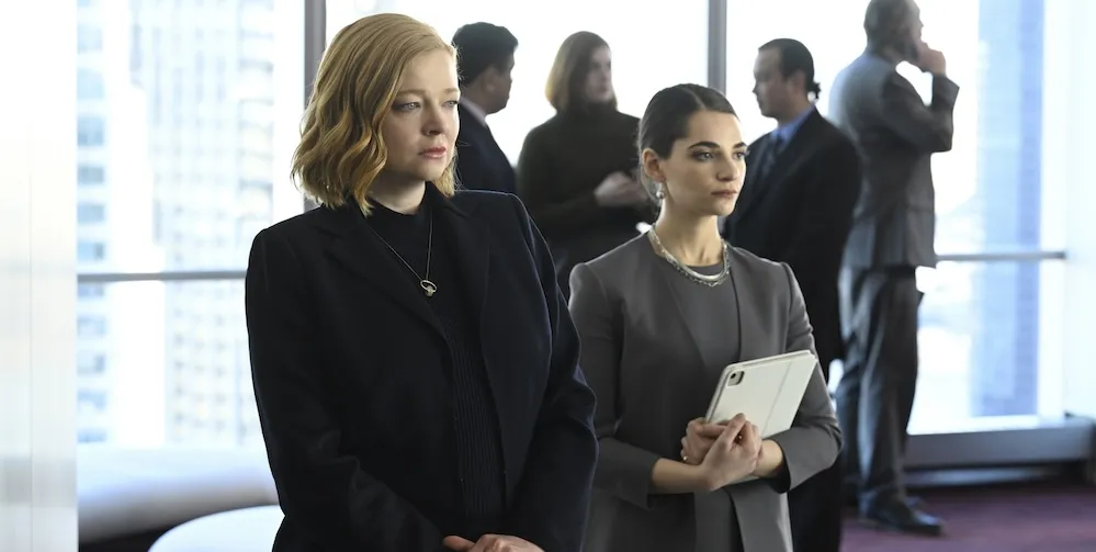 Two women in business suits looking ahead with a group of people behind them. 