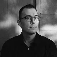 black and white photo of man with dark hair and glasses wearing a dark button up shirt