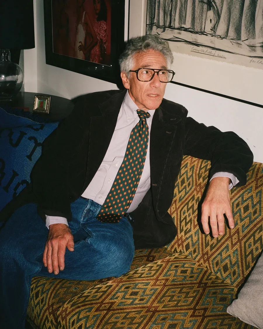 A man in a sports coat sits on a couch 