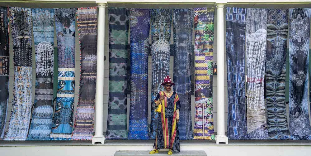 Woman standing in front of long banners with blue designs hanging in between white columns. 