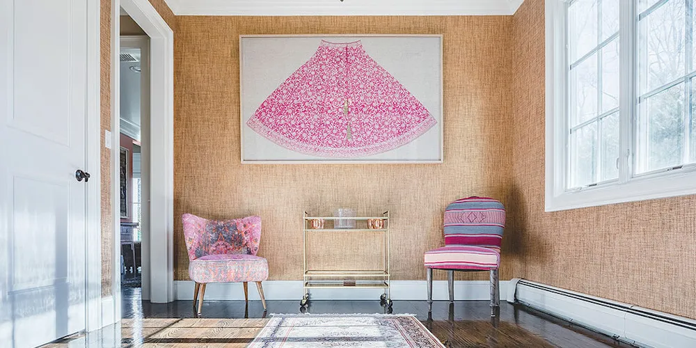 Shot of a room with two pink chairs, a decorative cart, and a framed skirt on the wall. 