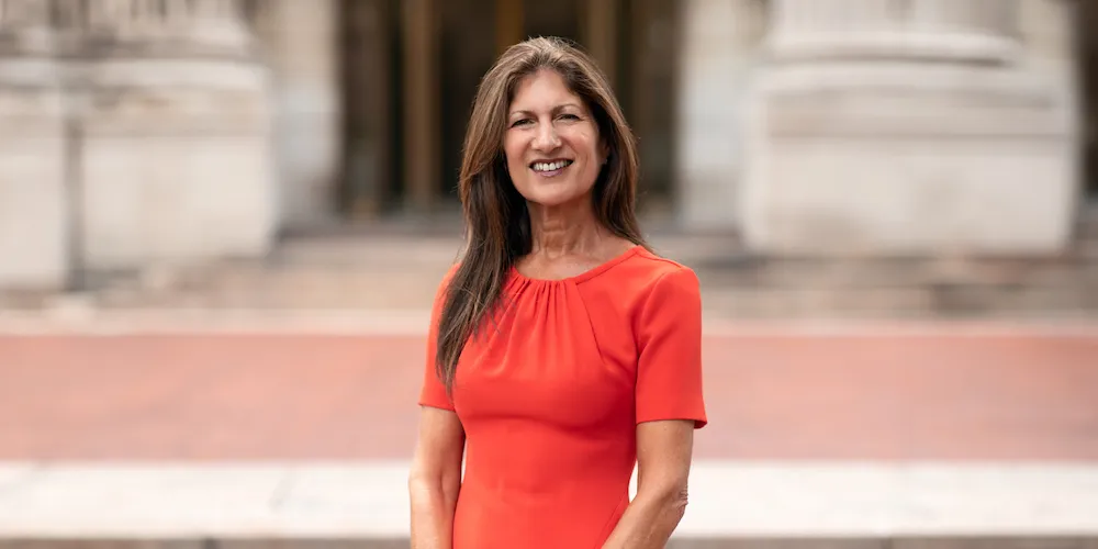 A woman in a red dress stands in front of a campus building. 