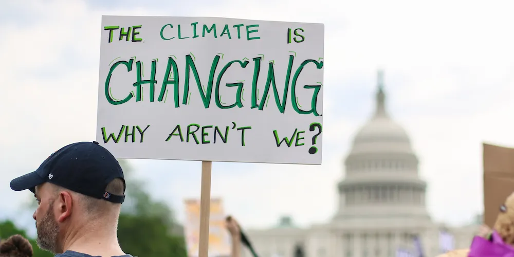 Man in baseball cap holds climate sign in front of the United States Capitol. 