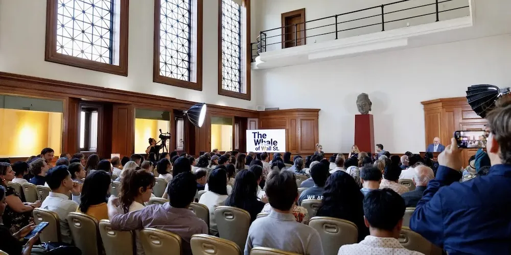 A crowd of people in a room listening to two speakers on stage. 