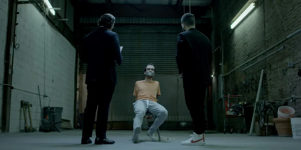 two men standing in front of seated hostage