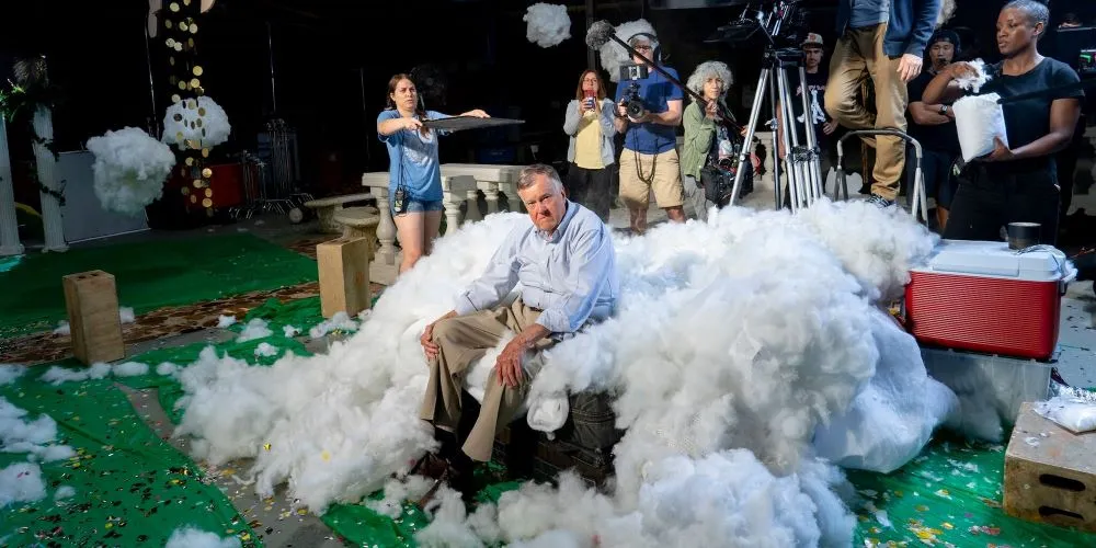 man sitting on film set surrounded by technicians