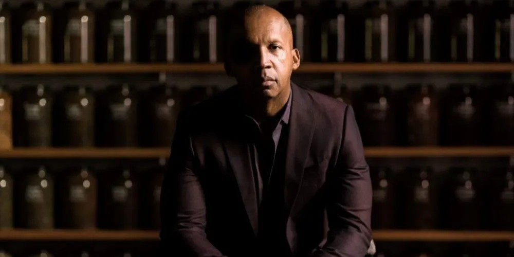 Black somber man sitting in a monochrome brown room. 
