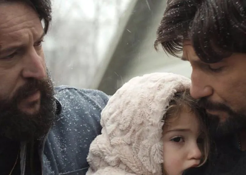 Two bearded men huddled around a young girl in the snow