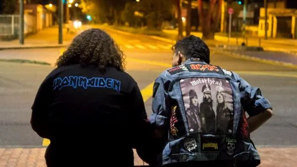 Two men in rock n roll jackets seated on curb