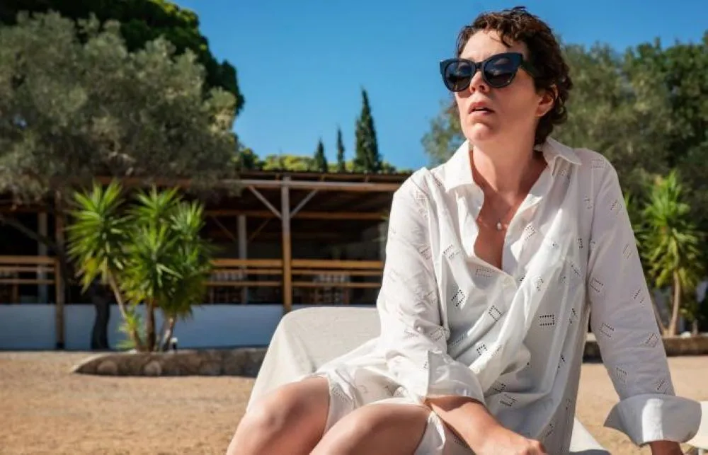 Woman in white shirt and sunglasses seated in an arid, outdoor setting