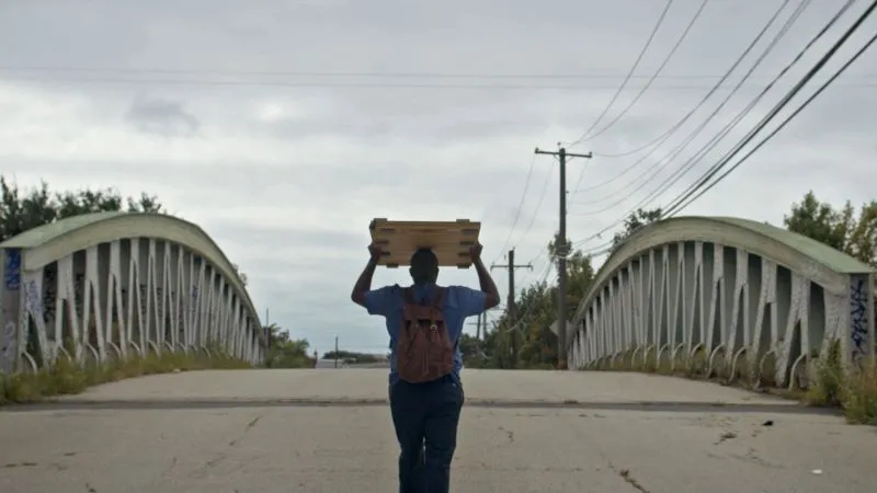 Man crossing bridge, carrying an object over his head