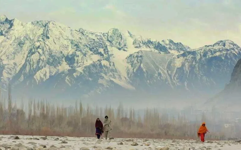 three people walking through plains with large snow-peaked mountains in the background