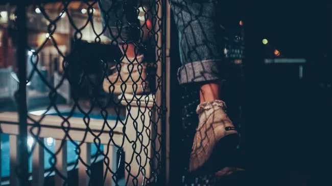 A shot of feet climbing over a metal fence