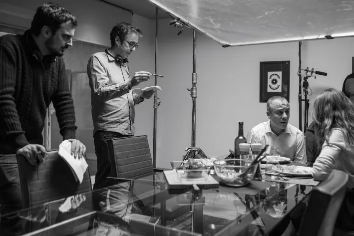 Director is talking to two actors seating at a dining table.