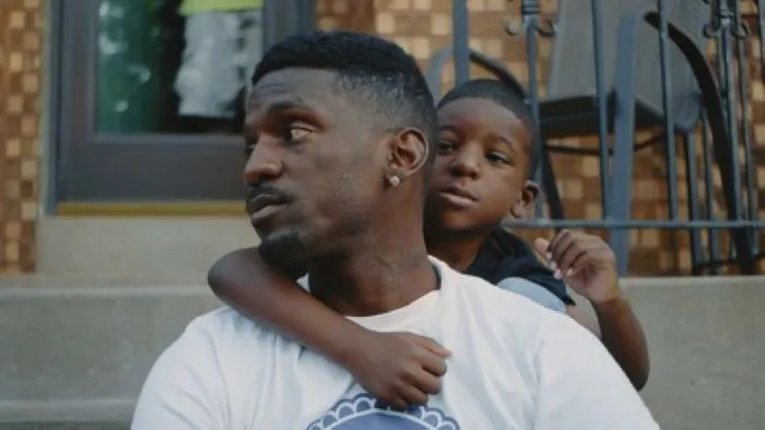 A man and a kid sit by the entrance of a house.