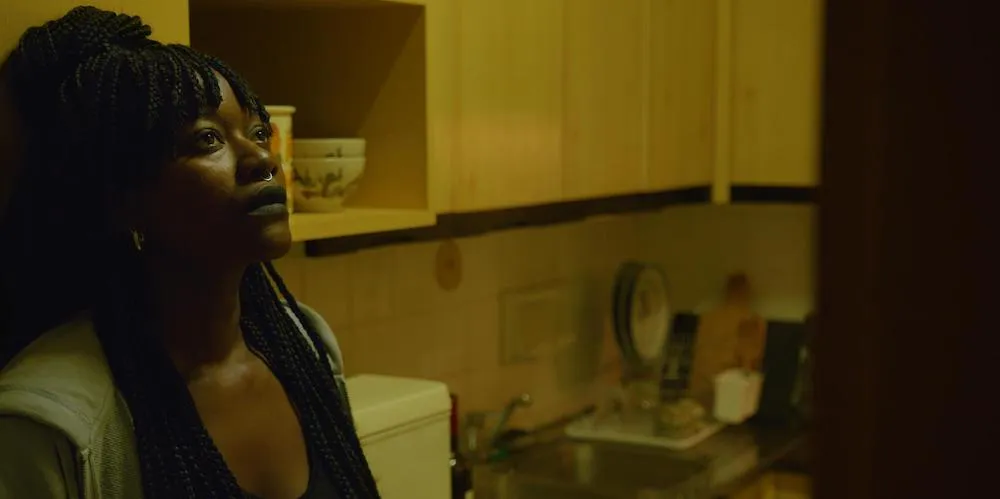 A woman leans against a wall in a kitchen, looking distressed. 