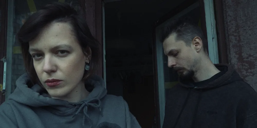 A woman (left) and a man (right) stand next to each other looking in different directions. 