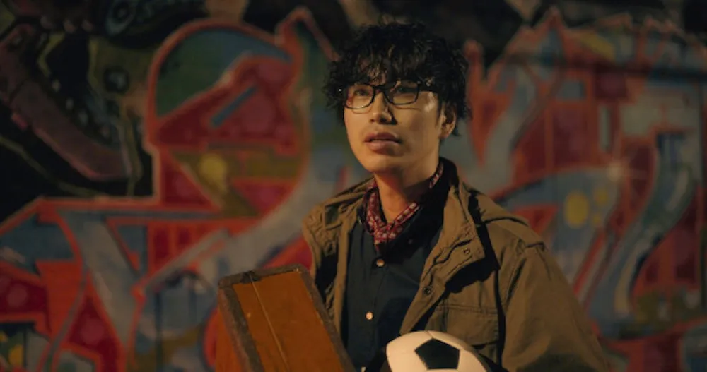  Man in front of graffitied wall holding a case and soccer ball
