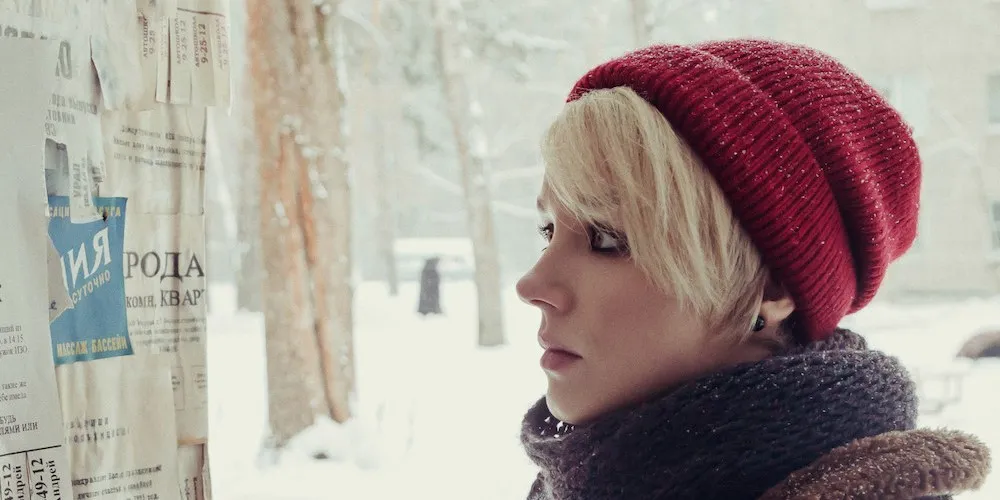 woman in snow looking at bulletin board of flyers in Cyrillic text