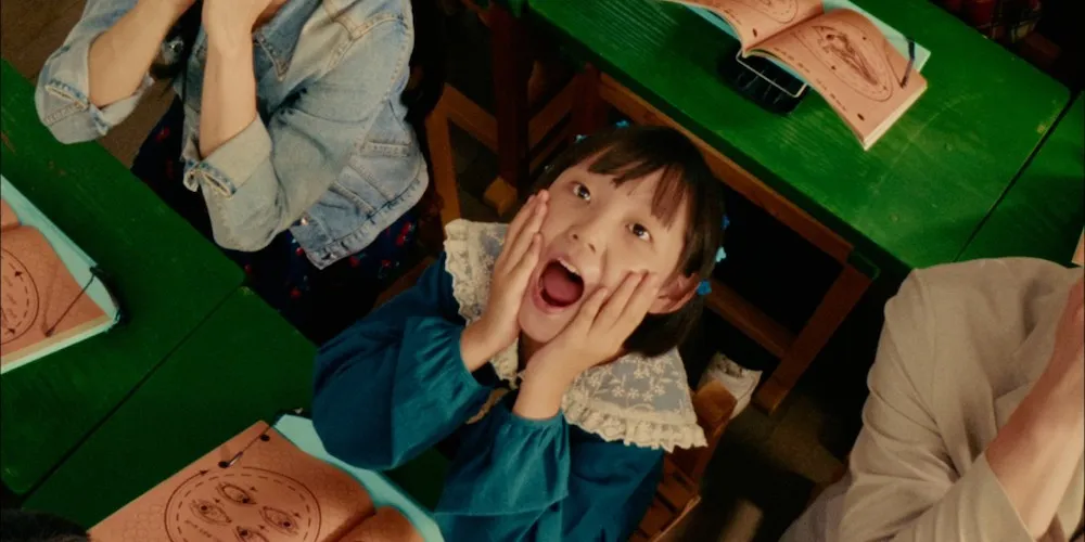 a young girl sits at a school desk with her hands on her face