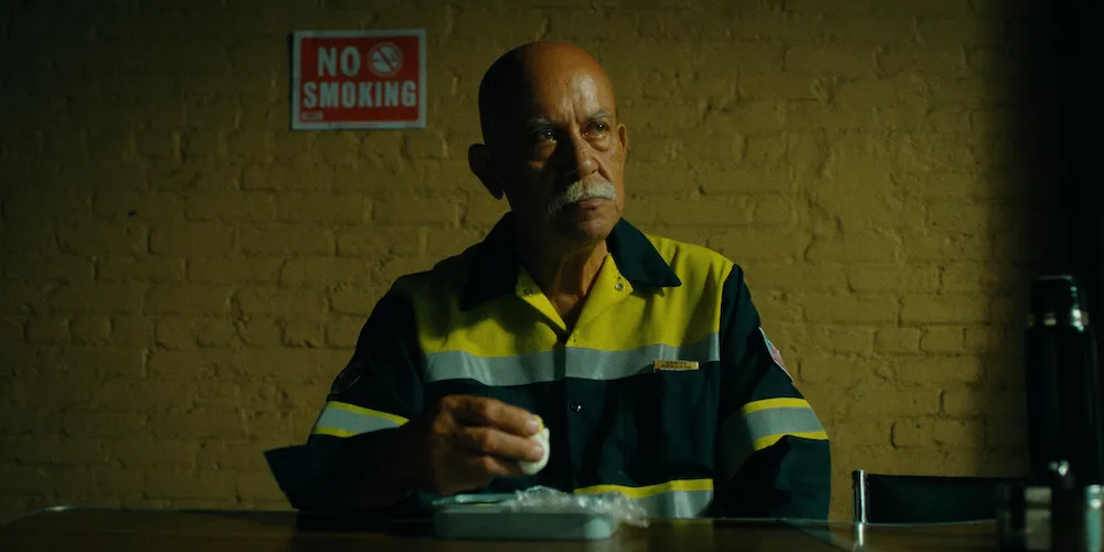 A man dressed in the uniform of a sanitation worker sits at a table eating a hard boiled egg