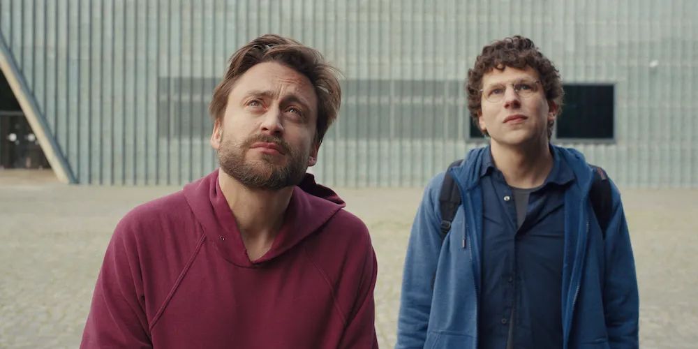 Two young men looking up at the sky in front of a modern building. 