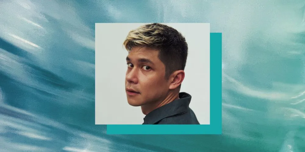Headshot of man with gray shirt on an aqua background. 