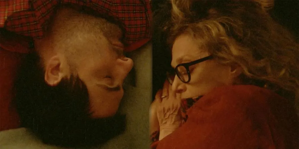 Two people lie in bed facing each other. 