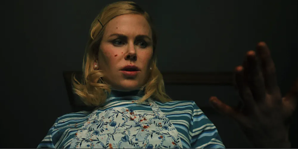 A woman with blood spattered on her face looks at her hand in horror. 
