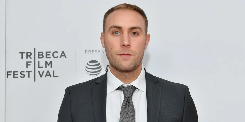 Man in gray suit standing in front of white background with Tribeca Film Festival logo. 