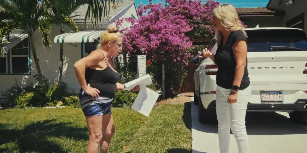 Two woman stand in a driveway. 