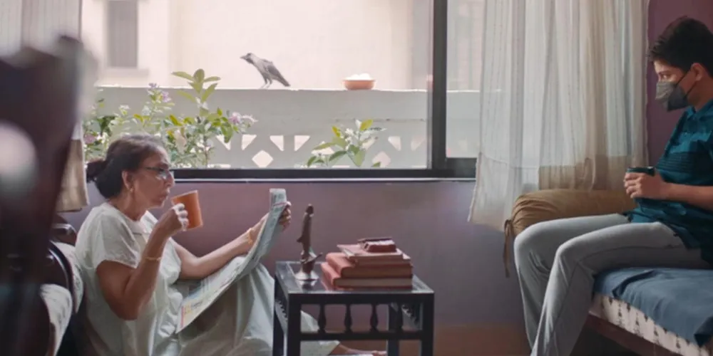 two people sit across from each other, one wearing a mask