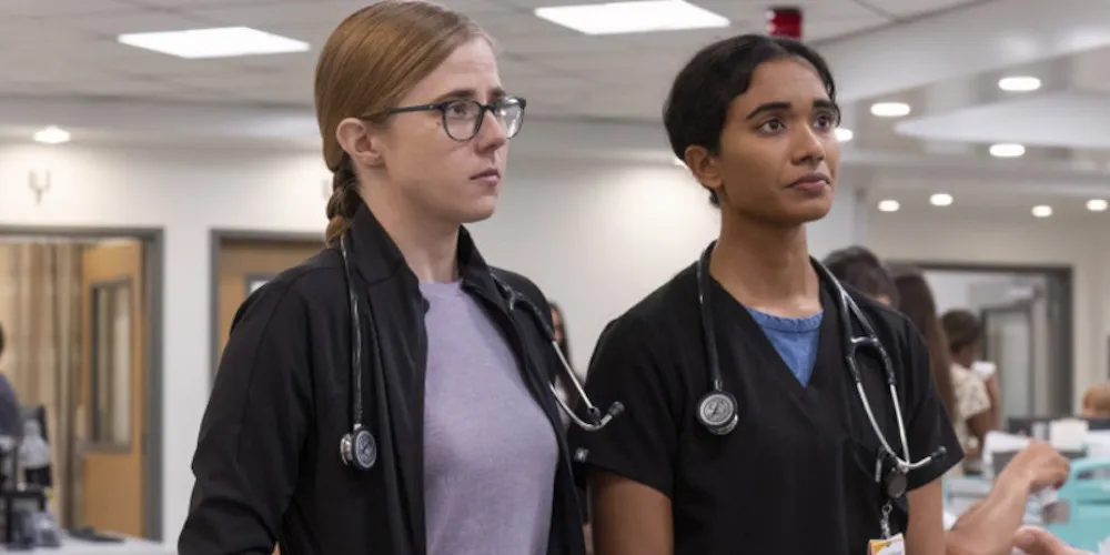 Two women in medical uniforms stand together in a hospital looking concerned. 