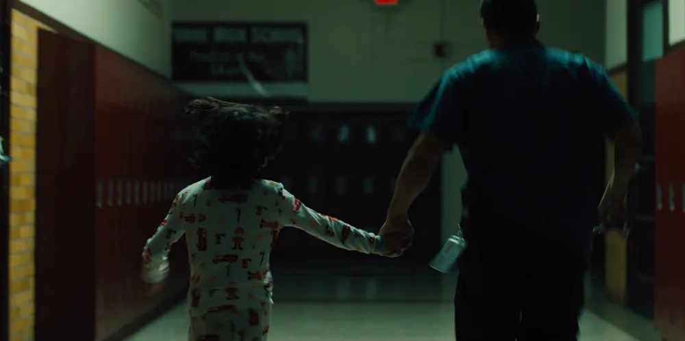an adult and child hold hands as they walk down a dim school hallway