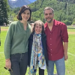 three people stand together outside, smiling