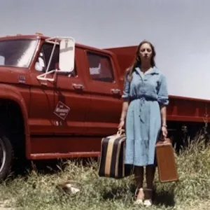 a woman holds two suitcases standing outside of a truck
