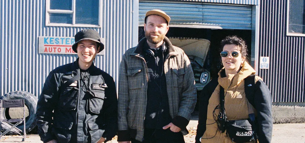 Three people stand smiling in front of building. 