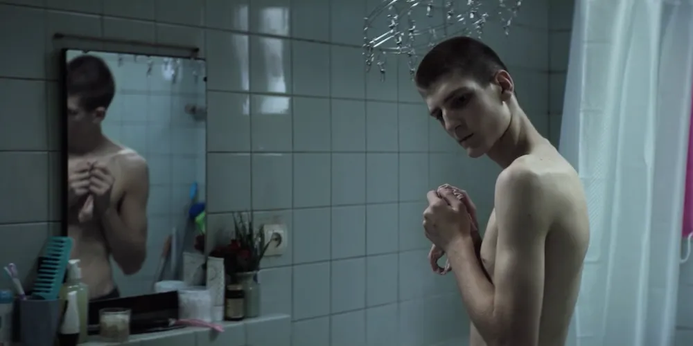 a young man stands in front of a bathroom mirror