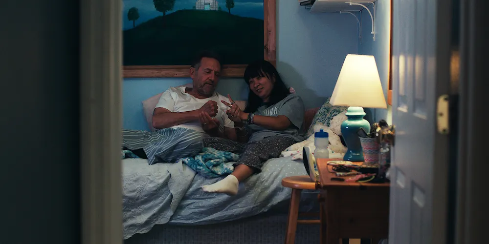 Two people sit in bed playing rock, paper, scissors. 