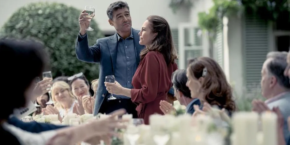 A man and woman stand outside at a crowded table toasting. 