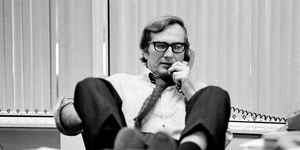 a man talks with his feet up on his desk talks on a landline phone