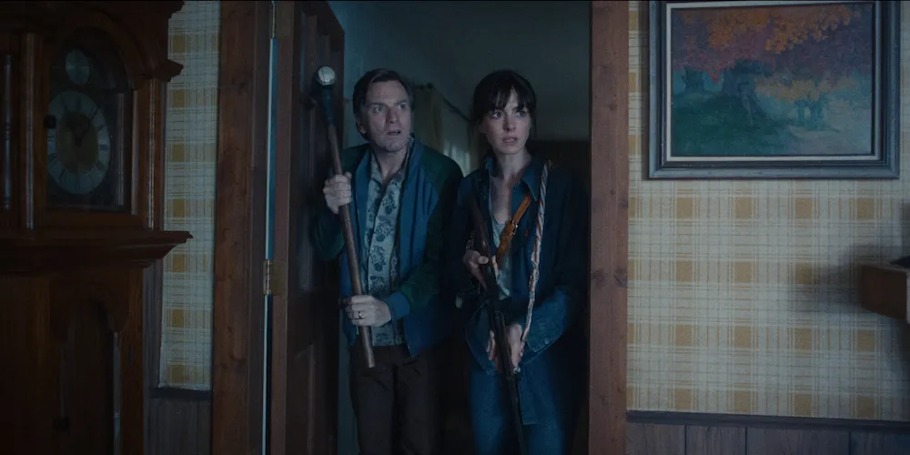 A man and woman stand in a doorway, each holding a gun.