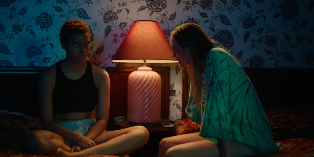 Two people sit on a bed. 