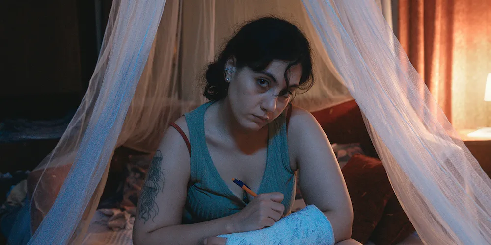 a person writes on a cast that covers their arm as they look at the camera