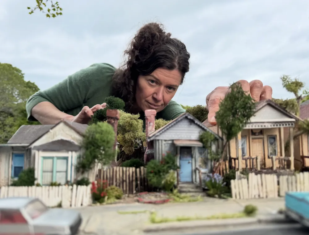 a woman peers over a miniature set of houses