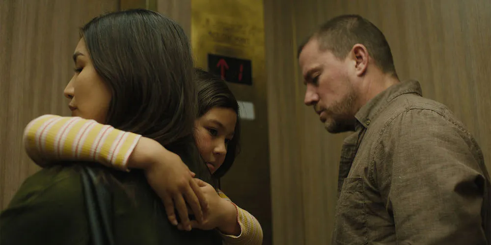 A woman holds a child in an elevator while a man stands behind them. 